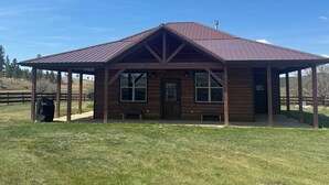 A single-story wooden building with a metal roof, a covered porch, and a fenced outdoor area. - Kara Creek Ranch - 2 Bed/2 Bath - Cabin 11 (Sundance)