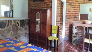 A room with a bed, a wooden wardrobe, a chair, a small table with a bowl, and a brick wall. - Capital O Posada Del Pescador Jocotepec (Coatzacoalcos)
