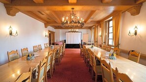 Ein Konferenzraum mit einem langen Tisch, Holzsesseln, einer Kristallleuchtre und Wandleuchten.