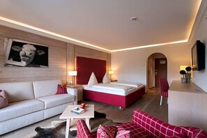 A modern hotel room with a sofa, a bed, a small table, and a red accent wall. - Hotel Gasthof Alte Post Holzkirchen (Holzkirchen)