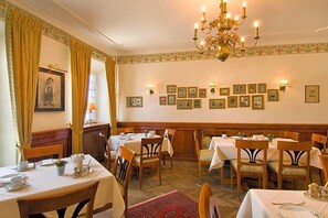 A dining area with tables set for service, a chandelier, and framed pictures on the wall. - Hotel Gasthof Alte Post Holzkirchen (Holzkirchen)