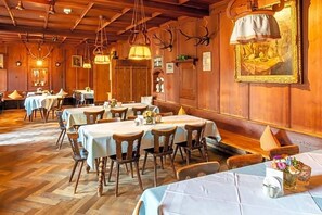 A restaurant with wooden walls, multiple tables, and hanging lights. - Hotel Gasthof Alte Post Holzkirchen (Holzkirchen)