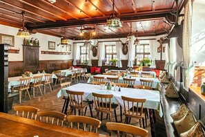 A dining area with wooden tables and chairs, hanging light fixtures, and windows with curtains. - Hotel Gasthof Alte Post Holzkirchen (Holzkirchen)
