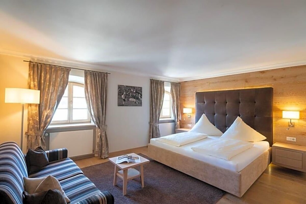 A hotel room with a bed, a sofa, a small table, and two bedside lamps.
