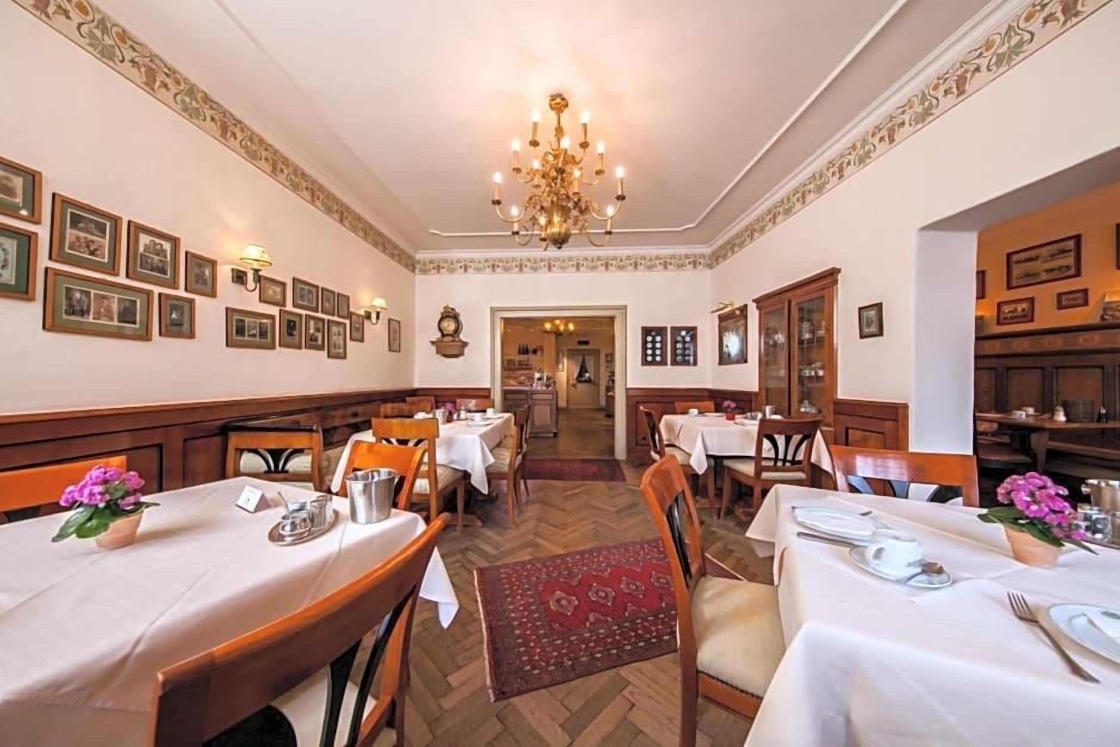 Ein formeller Speisesaal mit gedeckten Tischen, einem Kronleuchter, gerahmten Bildern an den Wänden und einem Fischgrätparkett.