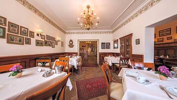Ein formeller Speisesaal mit gedeckten Tischen, einem Kronleuchter, gerahmten Bildern an den Wänden und einem Fischgrätparkett.