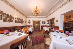 A formal dining room with tables set for service, a chandelier, framed pictures on the walls, and a herringbone floor pattern. - Hotel Gasthof Alte Post Holzkirchen (Holzkirchen)