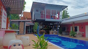 A pool area with a two-story building, a covered seating area, and a sign for a restaurant.
