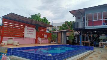 A swimming pool with blue tiles, a red fence, and a small building with a sign.