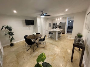 A dining area with a round table, chairs, a ceiling fan, and a TV mounted on the wall. - The Heights Retreat - Casa Azul at Cottage Grove (Houston)