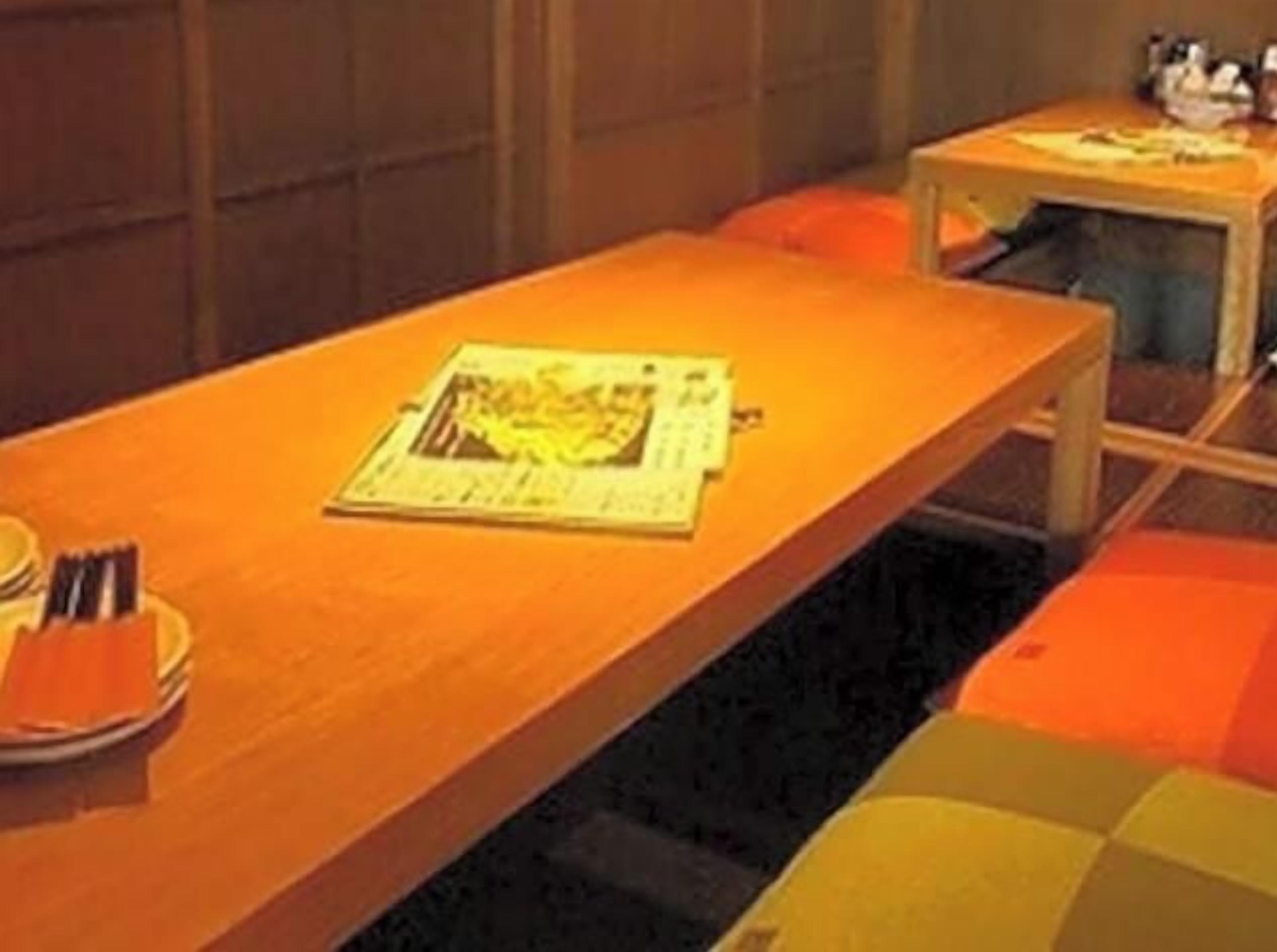 A room with a long table, a small table with a lamp, and orange seating.