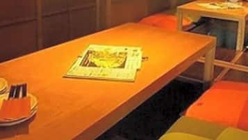 A room with a long table, a small table with a lamp, and orange seating.