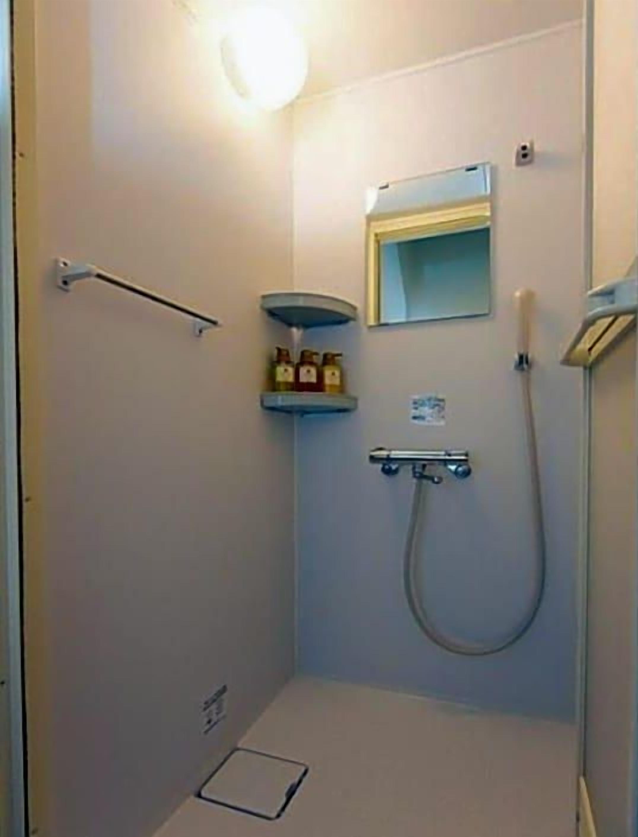 A small, enclosed shower area with a handheld showerhead, a wall-mounted mirror, and a shelf with toiletries.