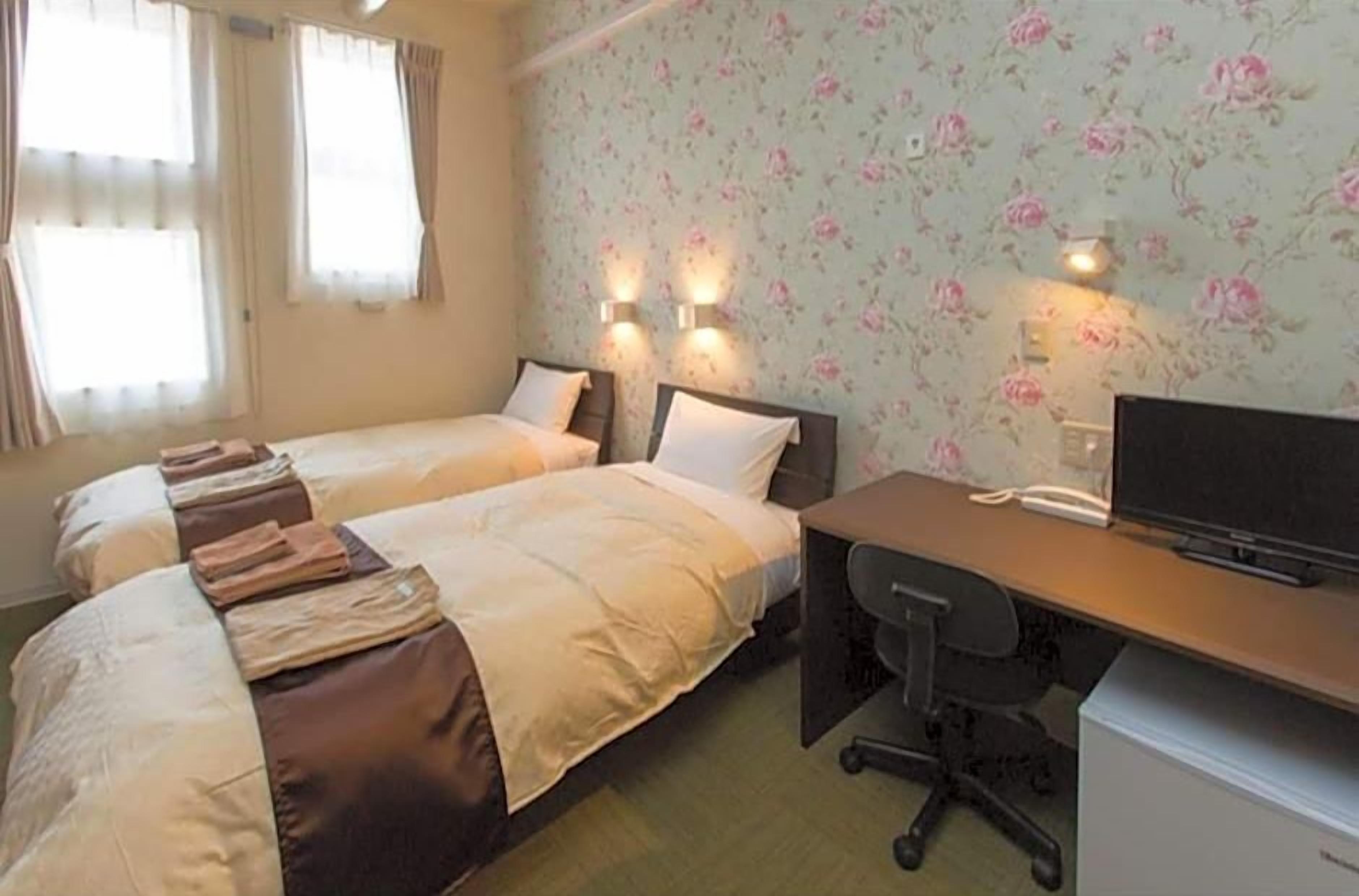 A hotel room with two beds, a desk, a chair, and a television.