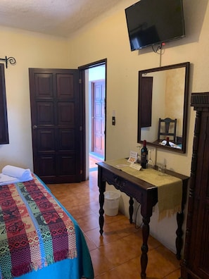 Een hotelkamer met een bed, een bureau met spiegel, een televisie en een deur naar buiten.
