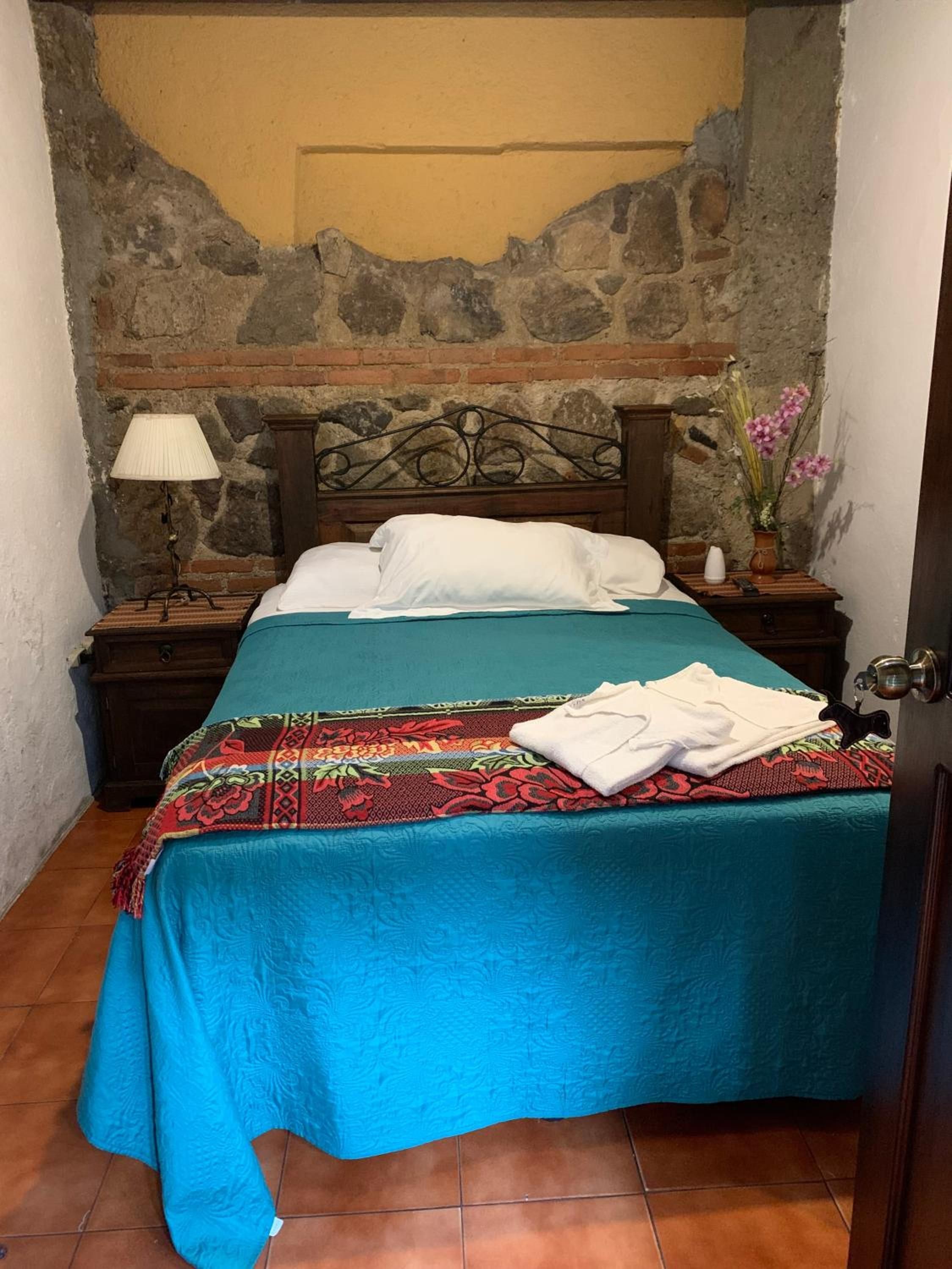A room with a bed, a nightstand, a lamp, and a vase with flowers.