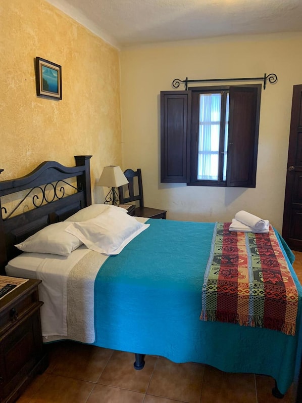 A bedroom with a bed, a nightstand, a lamp, a window with curtains, and a picture on the wall. - Hotel T Kon T (Antigua Guatemala)