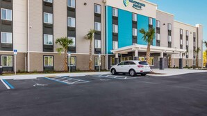A multi-story hotel with a flat facade, a blue accent wall, and a parking lot with marked handicapped spaces. - Woodspring Suites Jacksonville Campfield Commons (Jacksonville)