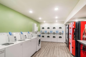 Une laverie équipée de plusieurs machines à laver et de plusieurs séchoirs, d’un distributeur de boissons Coca-Cola et d’un mur végétal.