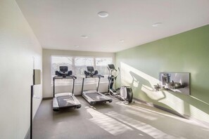 Un gimnasio con cintas de correr, una bicicleta estática y un dispensador de agua instalado en la pared.