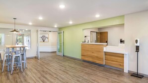 A modern reception area with a wooden reception desk, a glass partition, and a standing lamp. - Woodspring Suites Jacksonville Campfield Commons (Jacksonville)