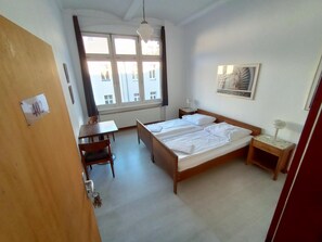 Une chambre d’hôtel avec un lit double, un bureau, une chaise, une table de chevet, une lampe et une fenêtre avec des rideaux.