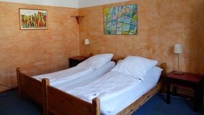 A single bed with white linens in a room with orange walls, two paintings, and two bedside tables with lamps.