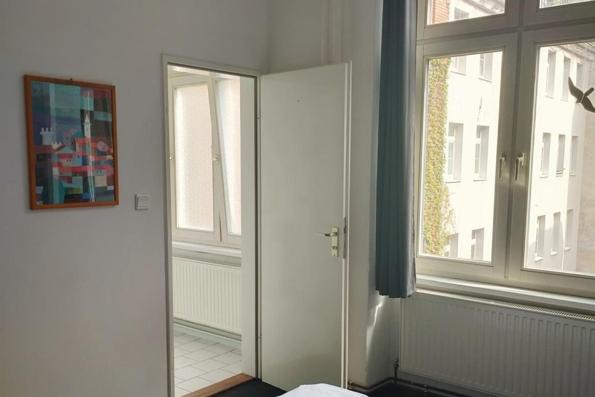 Ein Hotelzimmer mit zwei Betten, einem großen Fenster, einer Tür und einem Bild an der Wand.