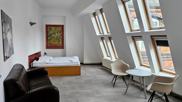 A modern room with a bed, a ceiling fan, a painting, a sofa, and a table with chairs.