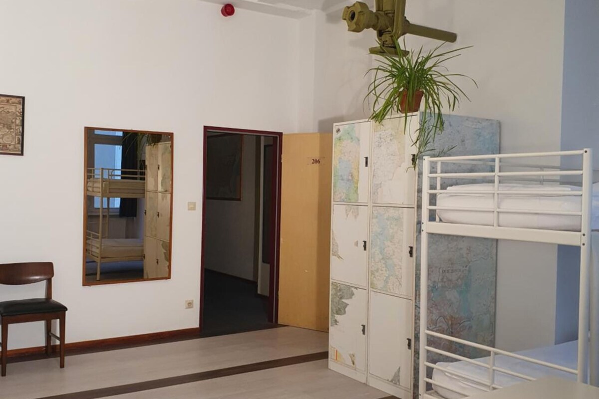 Une chambre avec des lits superposés, un bureau, une chaise, un luminaire suspendu et une carte accrochée au mur.