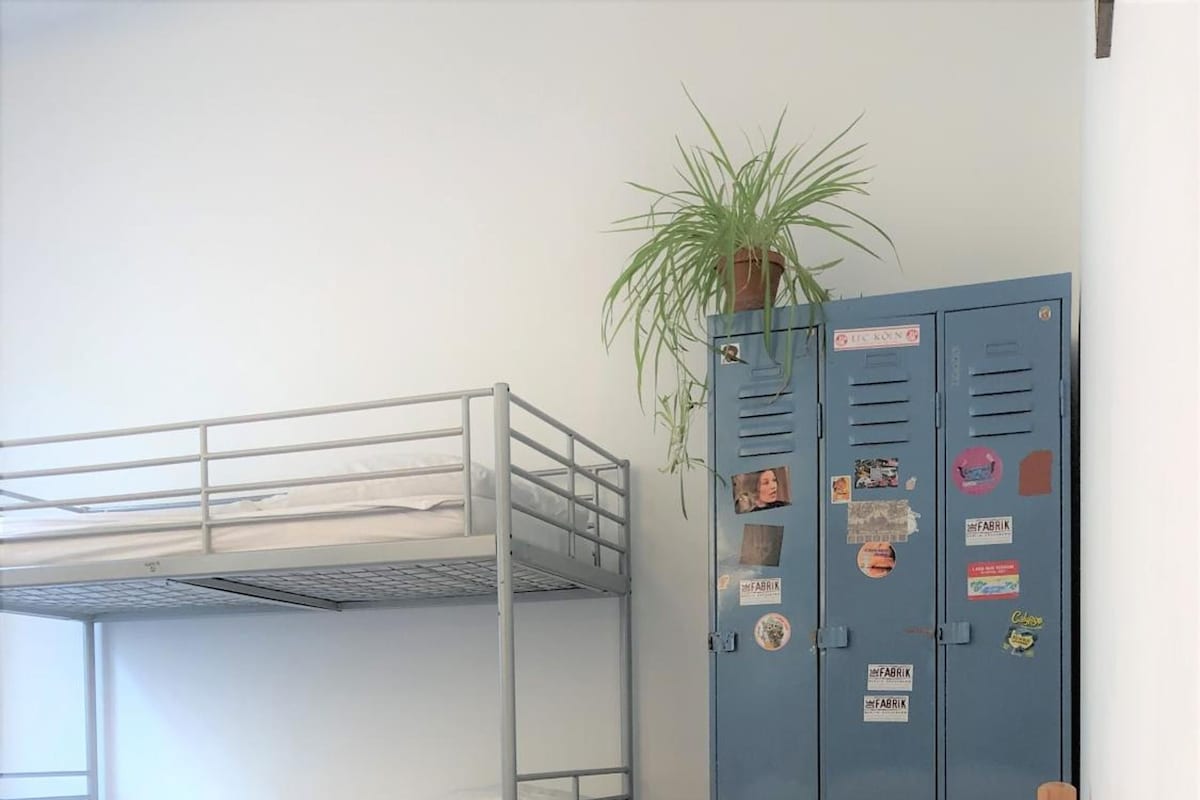 Ein Schlafzimmer mit Etagenbetten, einem Blumentopf, einem blauen Spind und einem hölzernen Kopfteil.