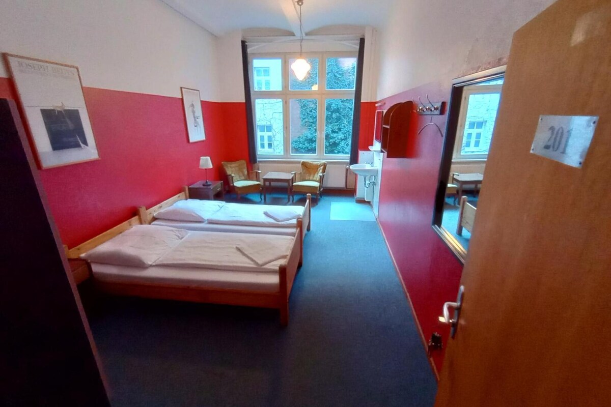 Une chambre d’hôtel avec deux lits, un bureau, une chaise, une fenêtre et une salle de bain.