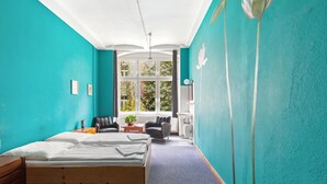 A room with a bed, two chairs, a small table, and a window with a view of trees.