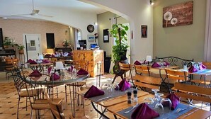A dining area with round tables, chairs, and purple napkins. There is a plant, a clock, and a wooden cabinet in the background. - Auberge De La Table Ronde (Vinon-sur-Verdon)