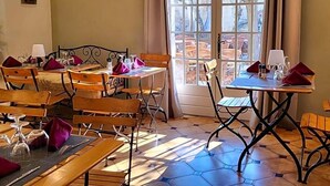 A dining area with wooden tables and chairs, a large window with a view, and a painting on the wall. - Auberge De La Table Ronde (Vinon-sur-Verdon)