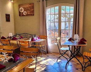 Zona pranzo con tavoli e sedie in legno, un'ampia finestra con vista e un quadro appeso al muro.