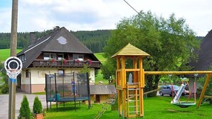 Une aire de jeux avec des balançoires, des structures d’escalade, un panier de basketball et une maison dotée d’un balcon.