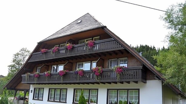 Un immeuble de deux étages, doté de balcons ornés de fleurs et de fenêtres, avec une voiture garée devant.