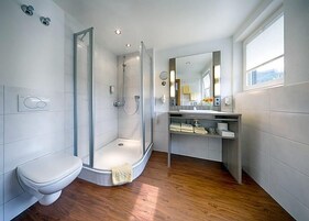 Ein modernes Badezimmer mit einer Duschkabine, Toilette, Waschbecken mit Spiegel und einem Fenster für Tageslicht.