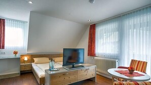 Une chambre d’hôtel moderne équipée d’un lit, d’une télévision, d’une table de chevet et d’un petit coin repas avec une table et des chaises.