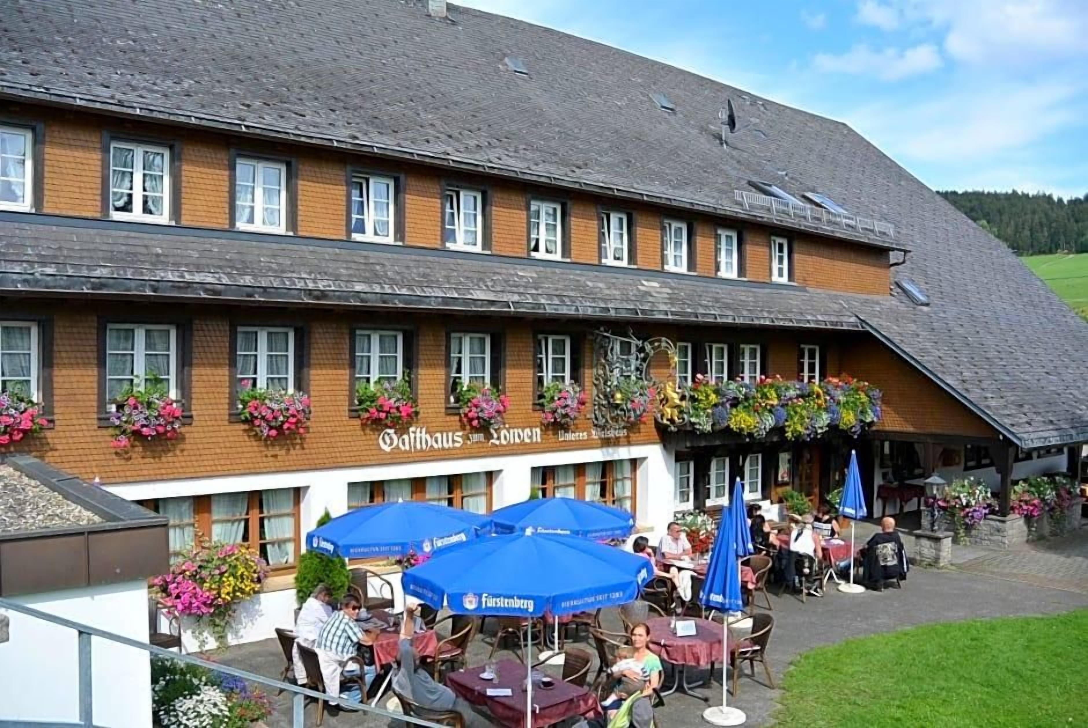 A traditional building with a sign reading 'Gaffhaus am Lofzen' and outdoor seating with blue umbrellas.