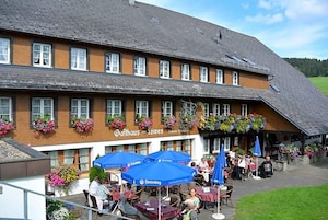Ein traditionelles Gebäude mit einem Schild, auf dem 'Gaffhaus am Lofzen' steht, und Außenbestuhlung mit blauen Sonnenschirmen.