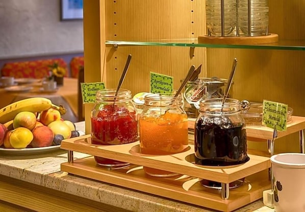 Un buffet de petit-déjeuner proposant une variété de confitures et de conserves, une assiette de fruits frais et un coin café.
