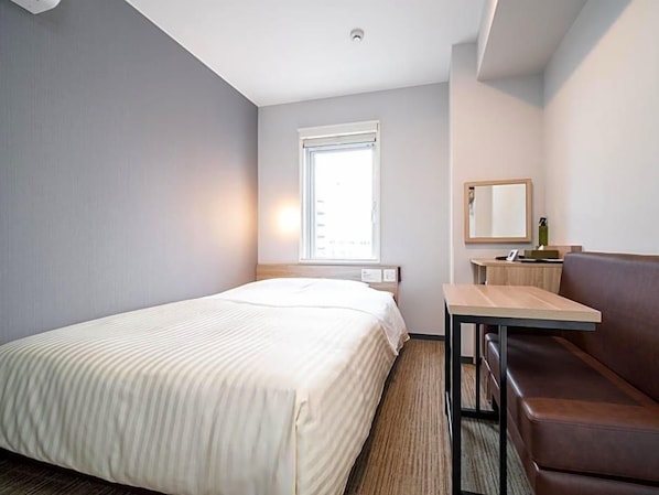 A hotel room with a bed, a small table, a sofa, a window, and a mirror. - Super Hotel Okayama Station Higashiguchi (Okayama)