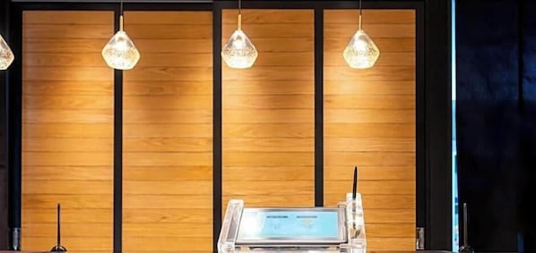 Een receptiebalie met een digitaal scherm, houten paneelachtergrond en hangende verlichting.
