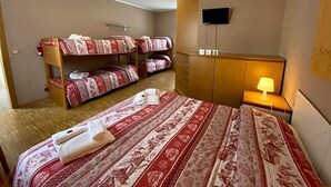 Ein Hotelzimmer mit Stockbetten, einem Flachbildfernseher, einer Nachttischlampe und einem Holzschrank.