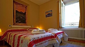 Une chambre d’hôtel avec deux lits, un grand tableau au mur, une fenêtre avec des rideaux et un radiateur.