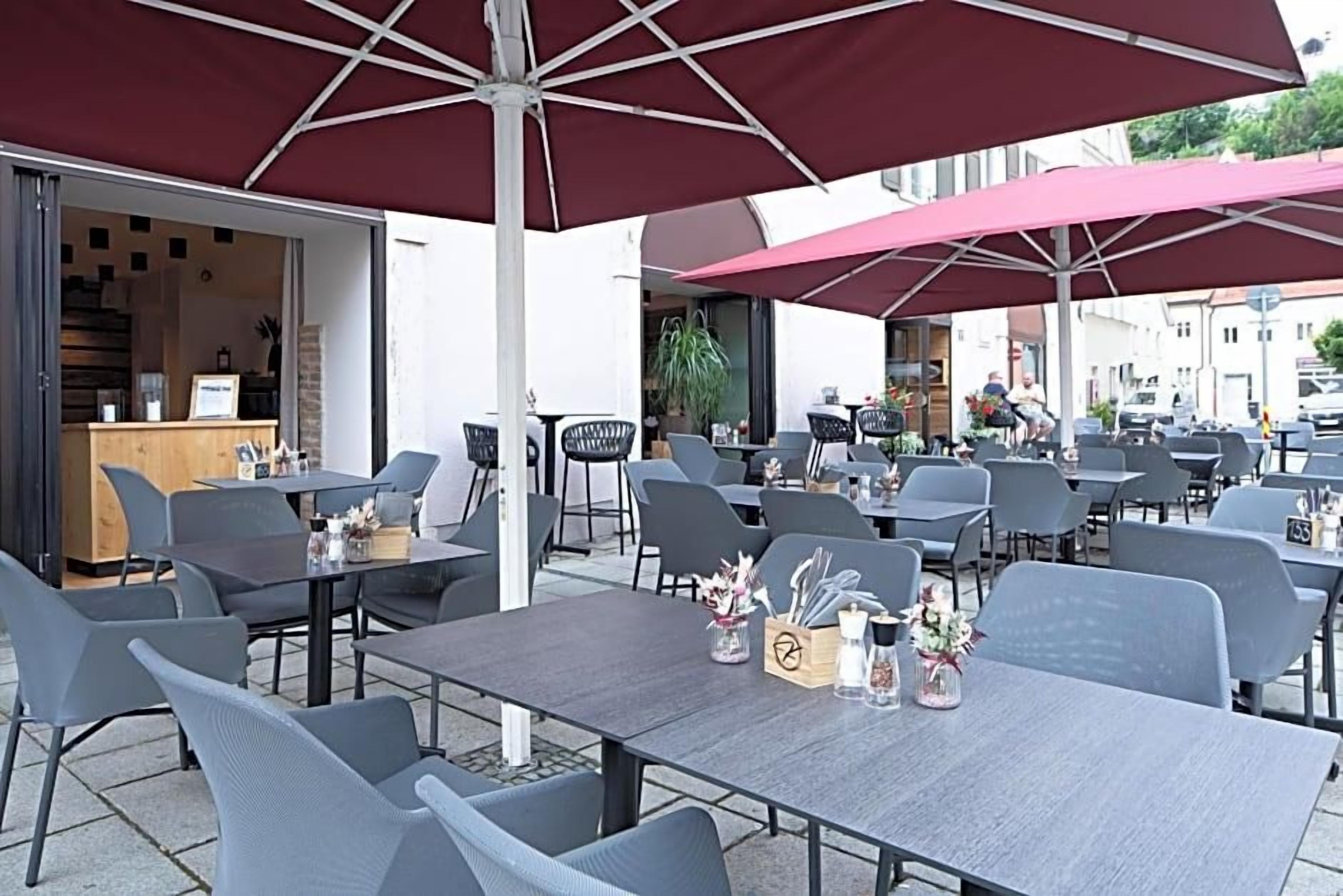 Ein Straßencafé mit Tischen, Stühlen, Sonnenschirmen und einer Theke mit Auslagen.