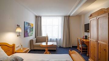 Ein Hotelzimmer mit Bett, Schreibtisch, Stuhl, kleinem Tisch, einer Couch, einem Fernseher und einem Kleiderschrank.