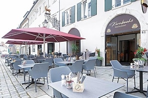 An outdoor café with tables and chairs, a red umbrella, and a restaurant sign. - Hotel Goldener Hirsch (Kaufbeuren)